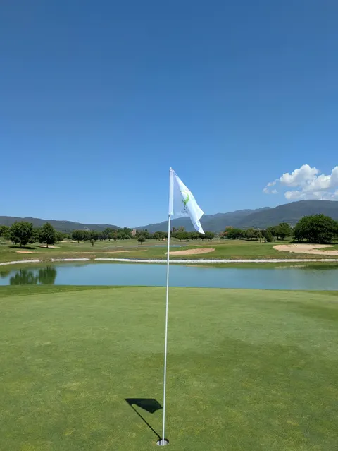 Bandera blanca al vent en un green, amb un llac i búnquers darrere